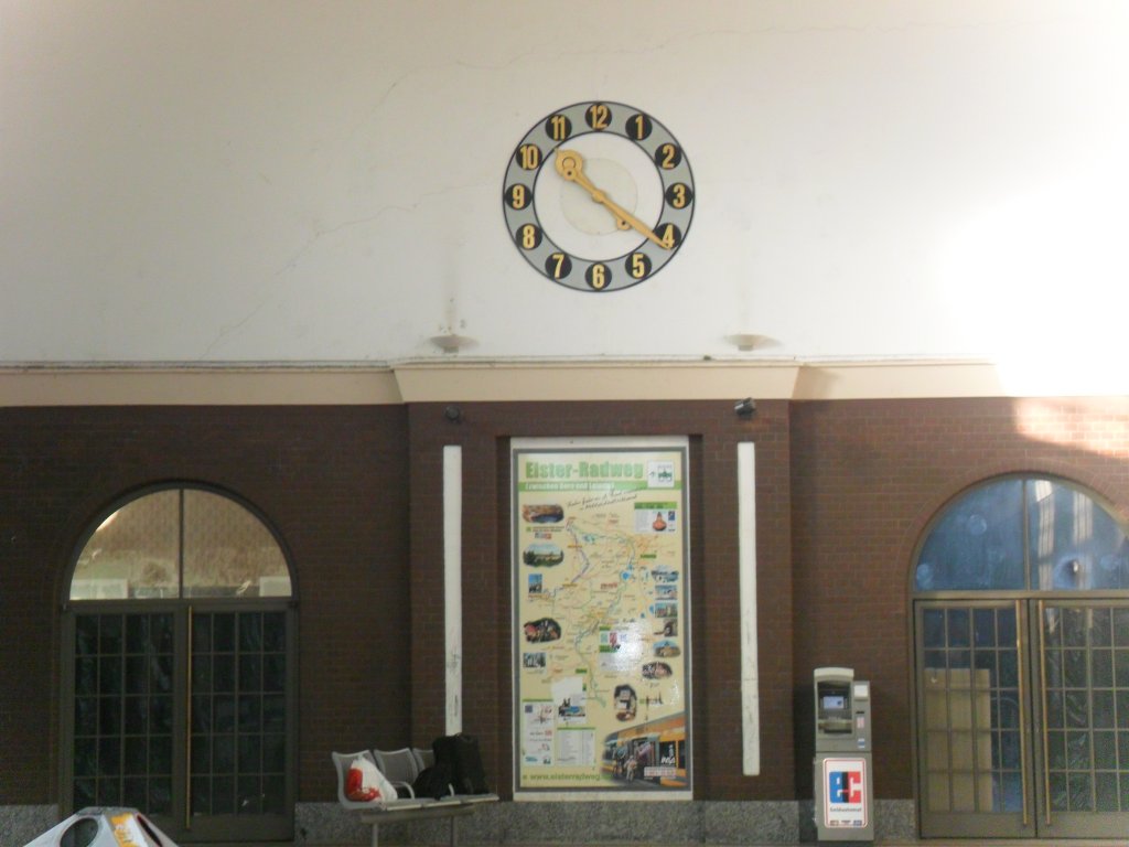 Die Sirnseite der Bahnhofshalle in Zeitz. Unter der Uhr wird fr den Elsterradweg geworben. Links ist der Eingang zur ehemaligen MITROPA Gaststtte zusehen. Die rechte Tr war der Eingang zum Wartesaal, wo auch die ehemalige MITROPA Selbstbedienungsgaststtte untergebracht war; 29.12.2011